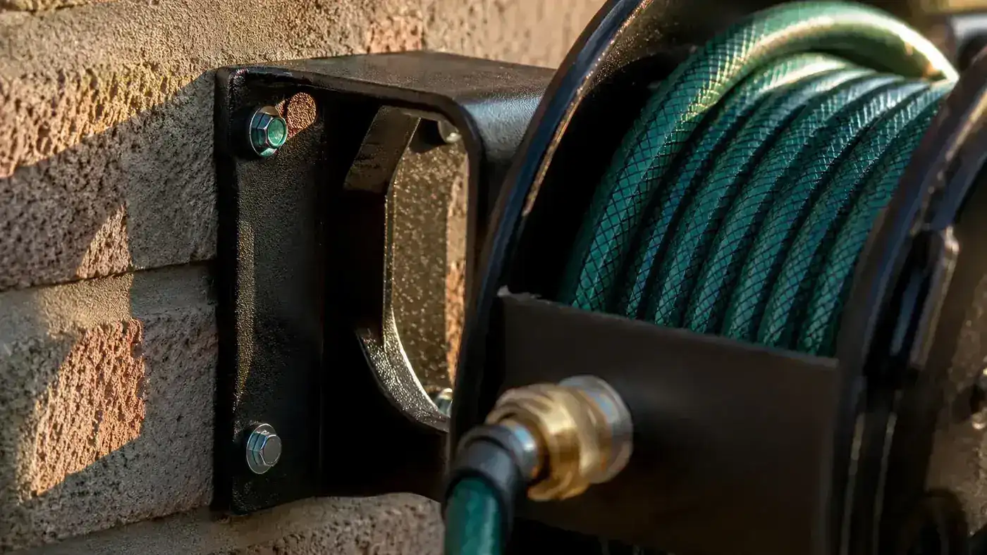 Close-up of retractable hose reel bracket mounted on brick wall showing masonry anchor bolts